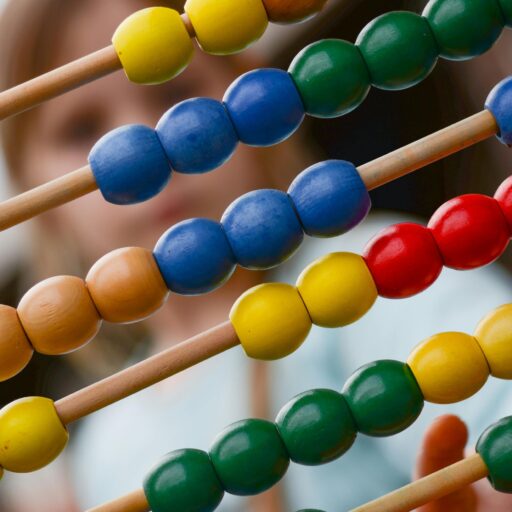 Close-up of colorful wooden abacus with a child learning math in the background, focusing on education and early childhood development.